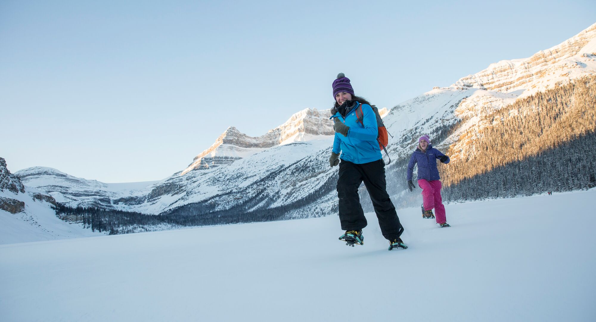Two people snowshoeing on Bow Lake in the winter with mountains in the background